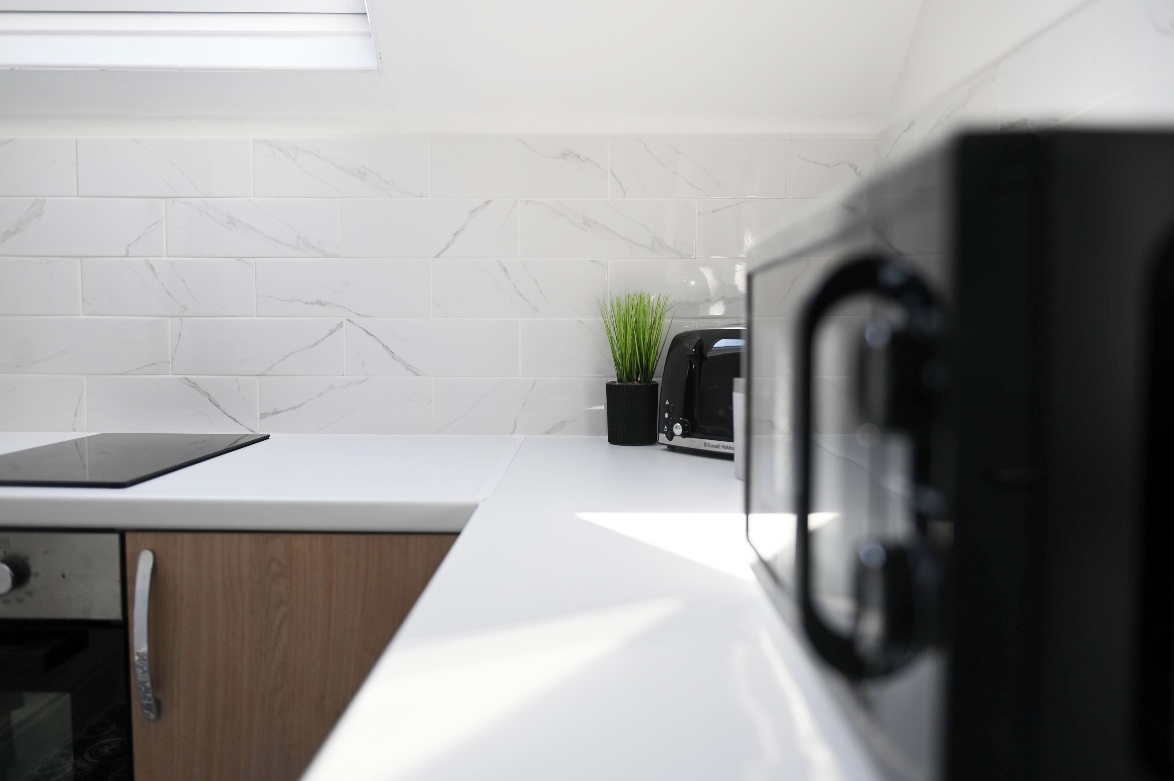 Une cuisine avec des carreaux de marbre blanc, un grille-pain noir, une petite plante en pot et une tablette posée sur le comptoir.