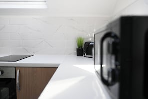 A kitchen with white marble tiles, a black toaster, a small potted plant, and a tablet on the counter.