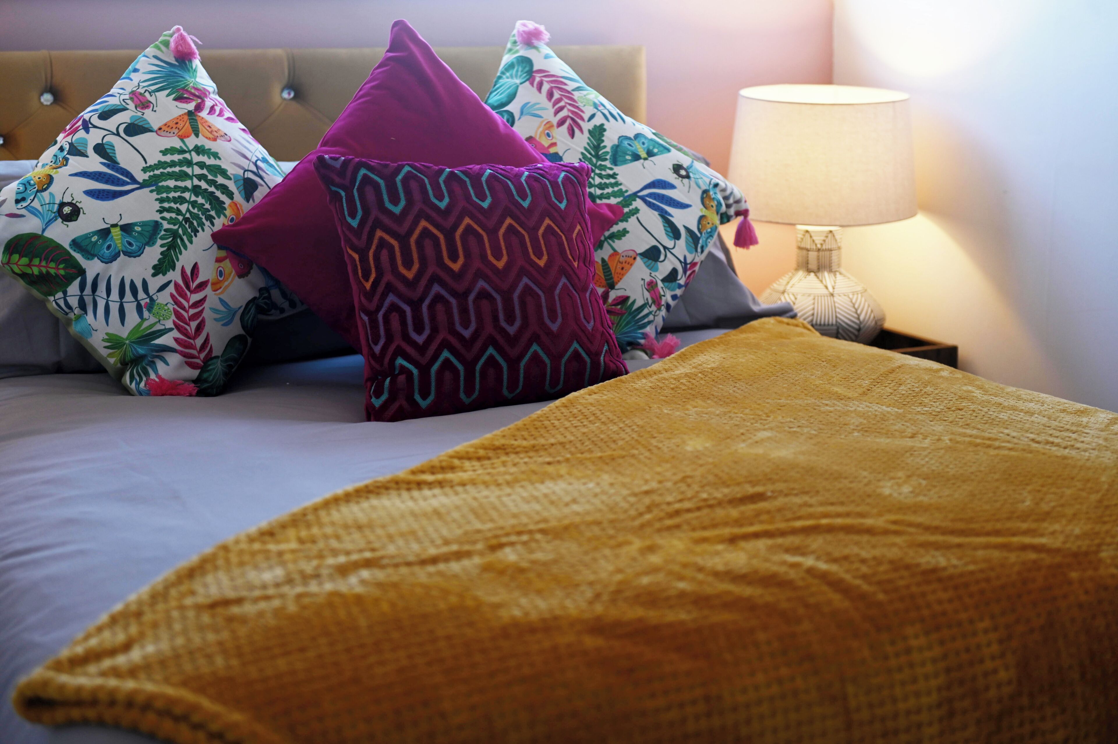 Un lit avec des coussins aux motifs colorés et une couverture de couleur moutarde.