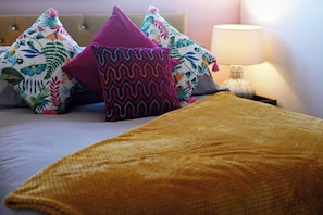 A bed with colorful patterned pillows and a mustard-colored blanket.