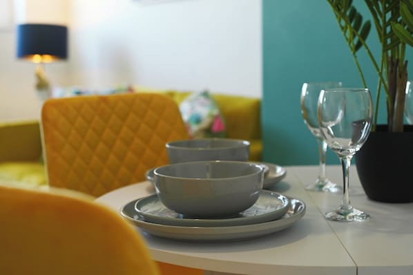A dining table with two bowls and a wine glass, set against a yellow chair and a teal wall.