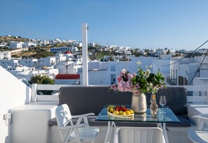 A balcony with a table set for two, featuring a fruit bowl, a vase with flowers, and a wine glass.
