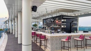 Un espace bar avec un comptoir et des tabourets de bar, un mur décoré de motifs et une vue sur la mer.