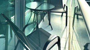 Un balcon moderne avec une paroi en verre, deux chaises et une petite table ronde.
