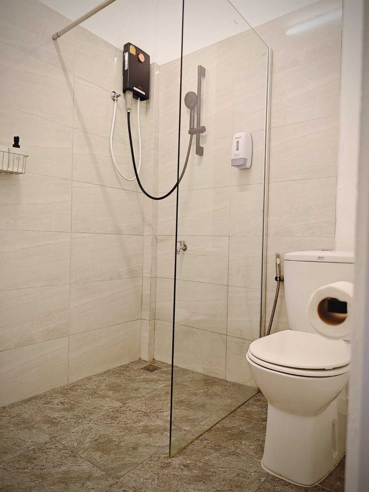 A modern bathroom with a glass-enclosed shower, a toilet, and a hand dryer.