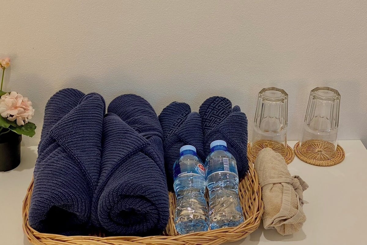 A basket with folded towels, two water bottles, and two empty glasses on a table.