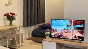 A hotel room with a bed, a desk, a chair, a TV displaying a beach scene, and a window with curtains. - homey stay and cafe by hematoa (Bangkok)