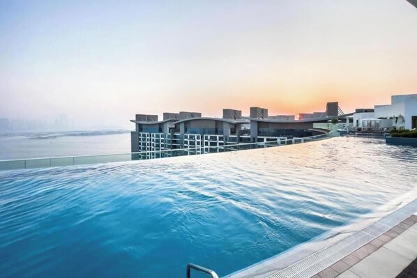 A rooftop infinity pool with a view of the city skyline at sunset.