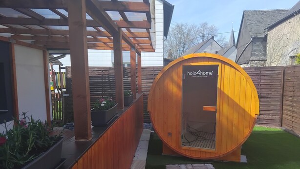 Una estructura de madera con una puerta que muestra el letrero "holz4home" en un patio trasero.