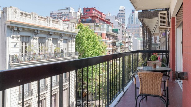 A balcony with a table and chairs, overlooking a cityscape with buildings and a tree. - MOT Juncal 2800 (Buenos Aires)