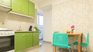 A kitchen with green cabinets, a white stove, and a dining area with a wooden table and turquoise chairs. - MOT Juncal 2800 (Buenos Aires)