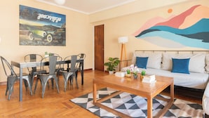 A modern living room with a dining area, featuring a sofa, coffee table, and a painting of a car on the wall. - MOT Juncal 2800 (Buenos Aires)
