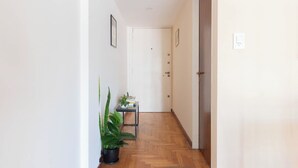 A hallway with a wooden floor, a potted plant, and a small table with books and a plant. - MOT Juncal 2800 (Buenos Aires)