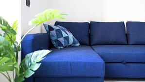 Un canapé d’angle bleu, agrémenté d’un coussin à motifs géométriques, est placé contre un mur blanc.