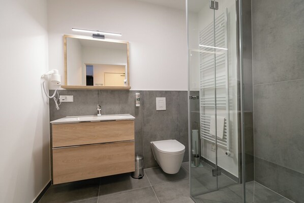 A modern bathroom with a wooden vanity, a toilet, and a glass shower enclosure.