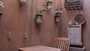 A wooden table and chair set against a textured wall with hanging planters containing flowers. - Vecchia Luna: Boutique Ground Floor, Val'Quirico. (Val'Quirico)