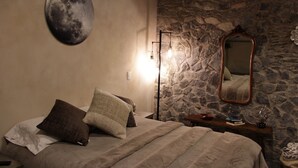 A bedroom with a stone wall, a round moon painting, a mirror, and a bedside table with books and a lamp. - Vecchia Luna: Boutique Ground Floor, Val'Quirico. (Val'Quirico)