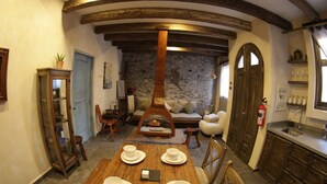 A dining area with a wooden table set for four, a stone wall, and a cozy seating area with a sofa and armchairs. - Vecchia Luna: Boutique Ground Floor, Val'Quirico. (Val'Quirico)