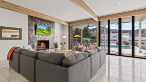 A modern living room with a large sectional sofa, a fireplace, and a view of a swimming pool and mountains.