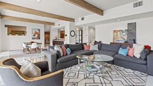 A modern living room with a sectional sofa, a glass coffee table, and a dining area in the background.