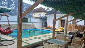 Un área de piscina con una silla hamaca, sillones reclinables y una mesa.