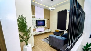A modern living room with a flat-screen TV, a sofa, a coffee table, and a potted plant.