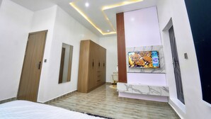 A modern bedroom with a bed, a TV mounted on the wall, wooden wardrobe, and a desk with a chair.