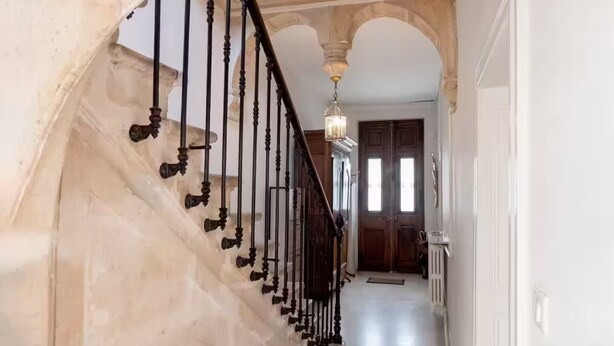 Una imponente escalera de diseño clásico que conduce a un pasillo bien iluminado con un gran pórtico al final.