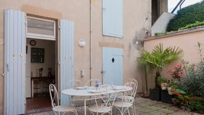 Un patio con una mesa y sillas de metal blanco, una puerta azul y plantas en macetas.