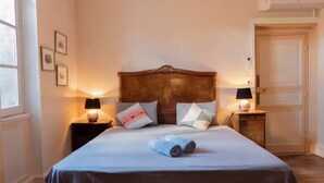 Una cama bien hecha con un edredón azul, dos lámparas de noche y un cabecero de madera.