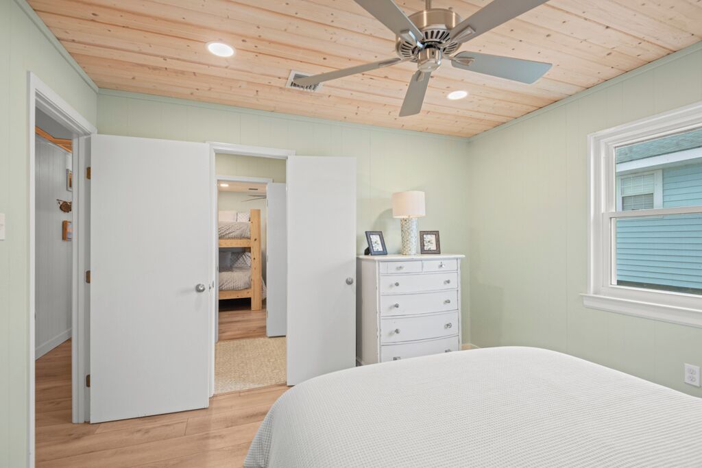A bedroom with a bed, a dresser, a ceiling fan, and a window.