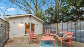 A small patio area with a white building, a glass door, and a seating arrangement including a table and chairs. - Charming Midtown Home w/ Private Patio; Mardi Gras (AL)