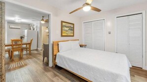 A bedroom with a bed, a ceiling fan, a desk with chairs, and a door. - Charming Midtown Home w/ Private Patio; Mardi Gras (AL)