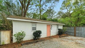 A single-story building with a white exterior, a red door, and a small porch area. - Charming Midtown Home w/ Private Patio; Mardi Gras (AL)
