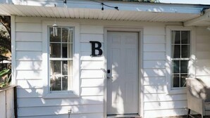 A white house with a door marked 'B', a porch, and a window. - Cozy Midtown Mobile Home; Fireplace & Pet-Friendly (AL)