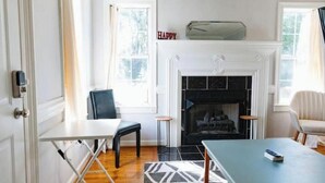 A room with a fireplace, a white door, a blue chair, a white table, and a patterned rug. - Cozy Midtown Mobile Home; Fireplace & Pet-Friendly (AL)