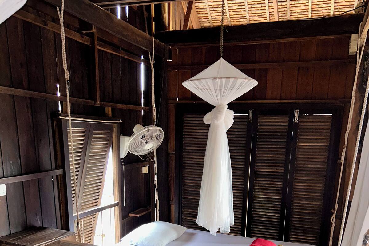 Une pièce rustique en bois, avec un lit, une moustiquaire suspendue et une petite table.