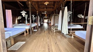 Een lange gang met meerdere bedden, elk voorzien van een hemelbed en een ventilator.