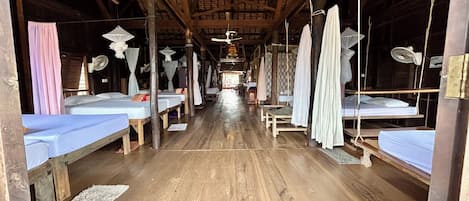 A long corridor with multiple beds, each with a canopy and a fan.