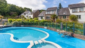 A swimming pool with a wavy edge design, surrounded by a fence and a row of houses. - Pet Friendly Luxury 5* 2 Bedroom Cottage with Hot Tub - Haven (Truro)