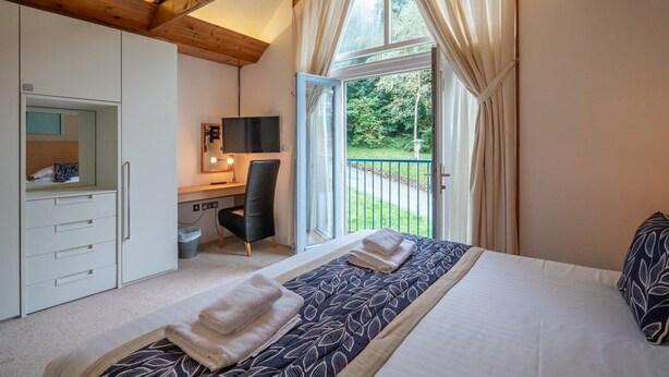 A bedroom with a large bed, a desk, and a chair, a wardrobe, and a window with curtains. - Pet Friendly Luxury 5* 2 Bedroom Cottage with Hot Tub - Haven (Truro)