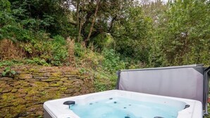 A hot tub in an outdoor setting with a stone wall and greenery in the background. - Pet Friendly Luxury 5* 2 Bedroom Cottage with Hot Tub - Haven (Truro)