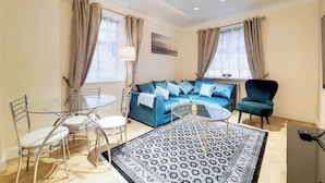 A modern living room with a blue sofa, a glass coffee table, and a patterned rug. - Quebec Residence (London)