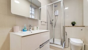 A modern bathroom with a glass-enclosed shower, a white toilet, and a vanity with toiletries. - Quebec Residence (London)