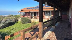 A covered outdoor area with a wooden deck, a stone pathway, and a view of a building with solar panels.