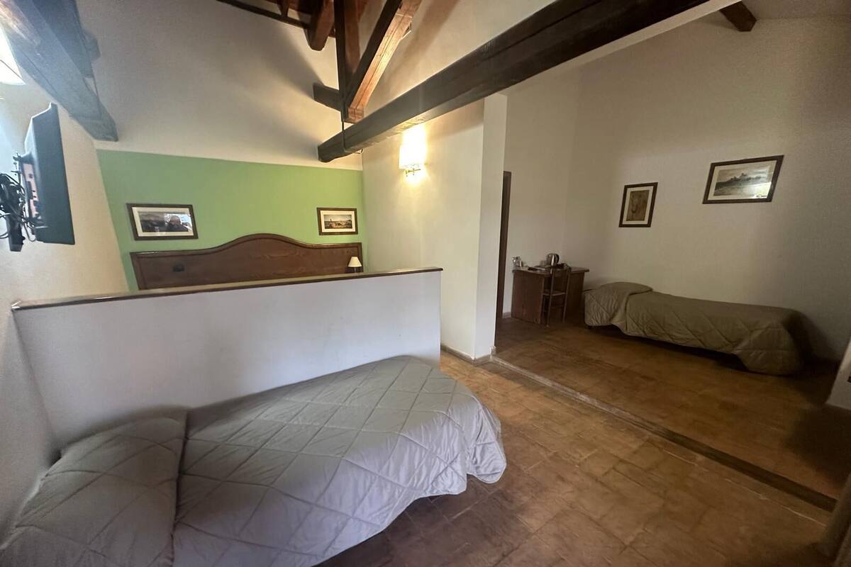 Een kamer met een bed, een klein tafeltje en een stoel. Er hangt een foto aan de muur en op het tafeltje staat een lamp.
