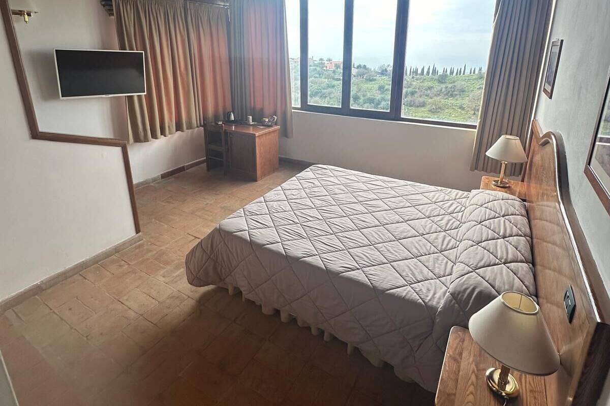 Een slaapkamer met een groot bed, een televisie, een bureau en uitzicht op de omgeving.