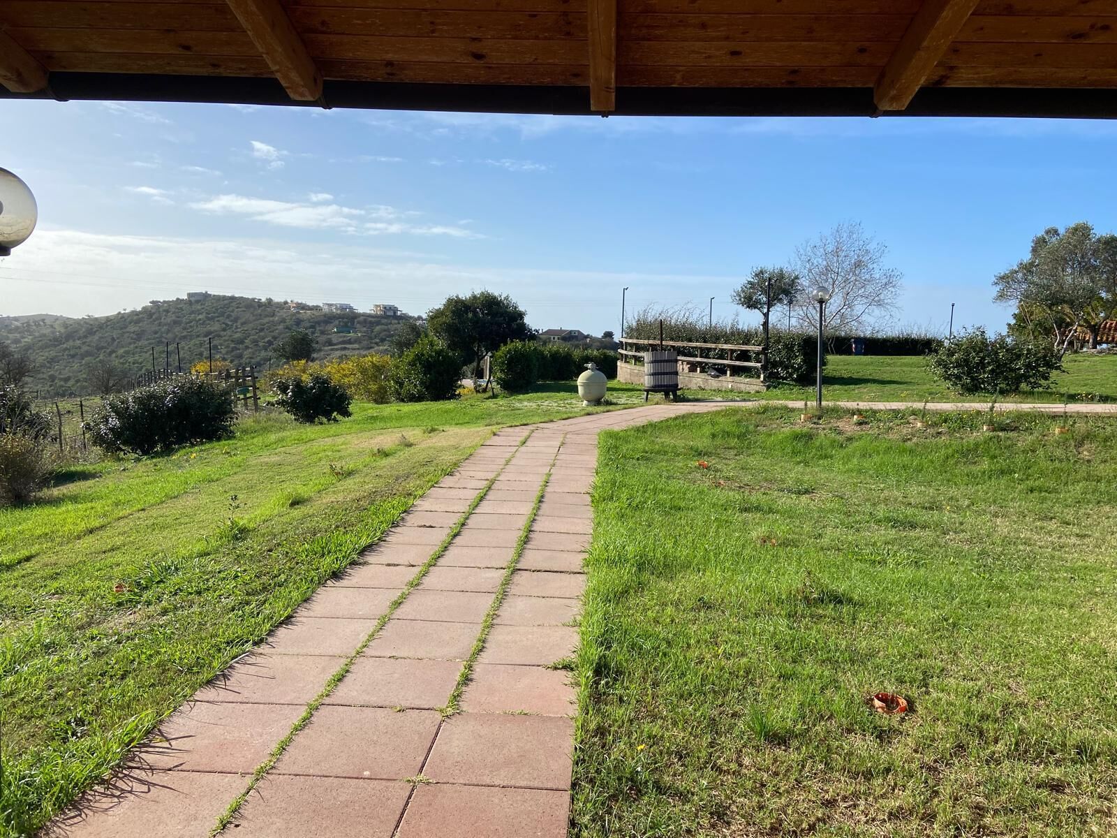 A paved pathway leading through a grassy area with a wooden shelter overhead.
