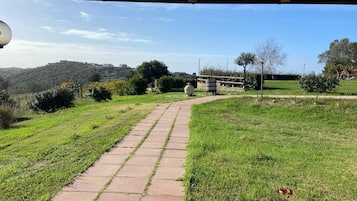 A paved pathway leading through a grassy area with a wooden shelter overhead.