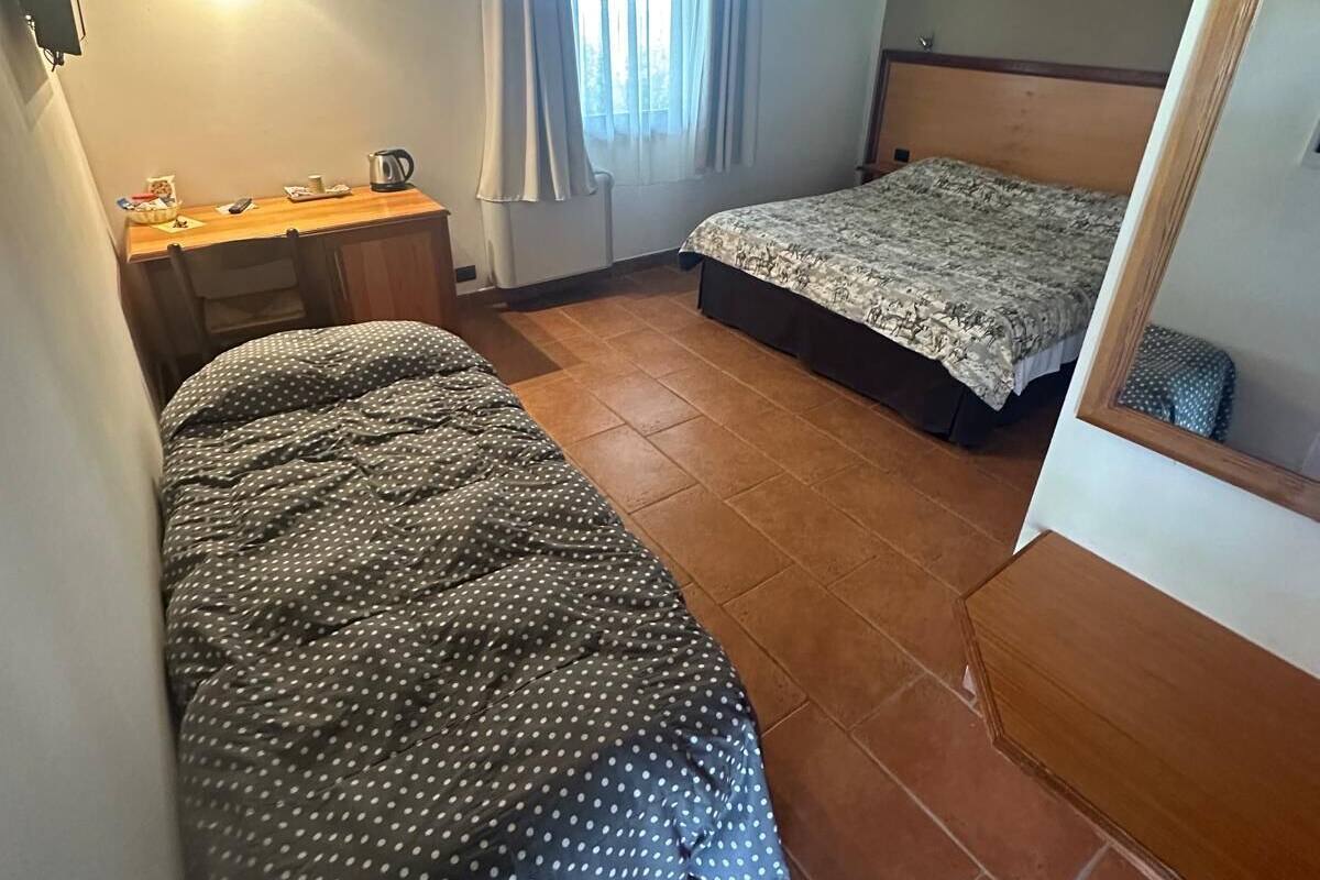 Een ruime, goed verlichte kamer met twee bedden, een houten bureau en een raam met gordijnen.